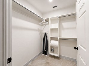 Ein begehbarer Kleiderschrank mit offenen Regalen, einer Kleiderstange und einem zusammengeklappten Bügelbrett.