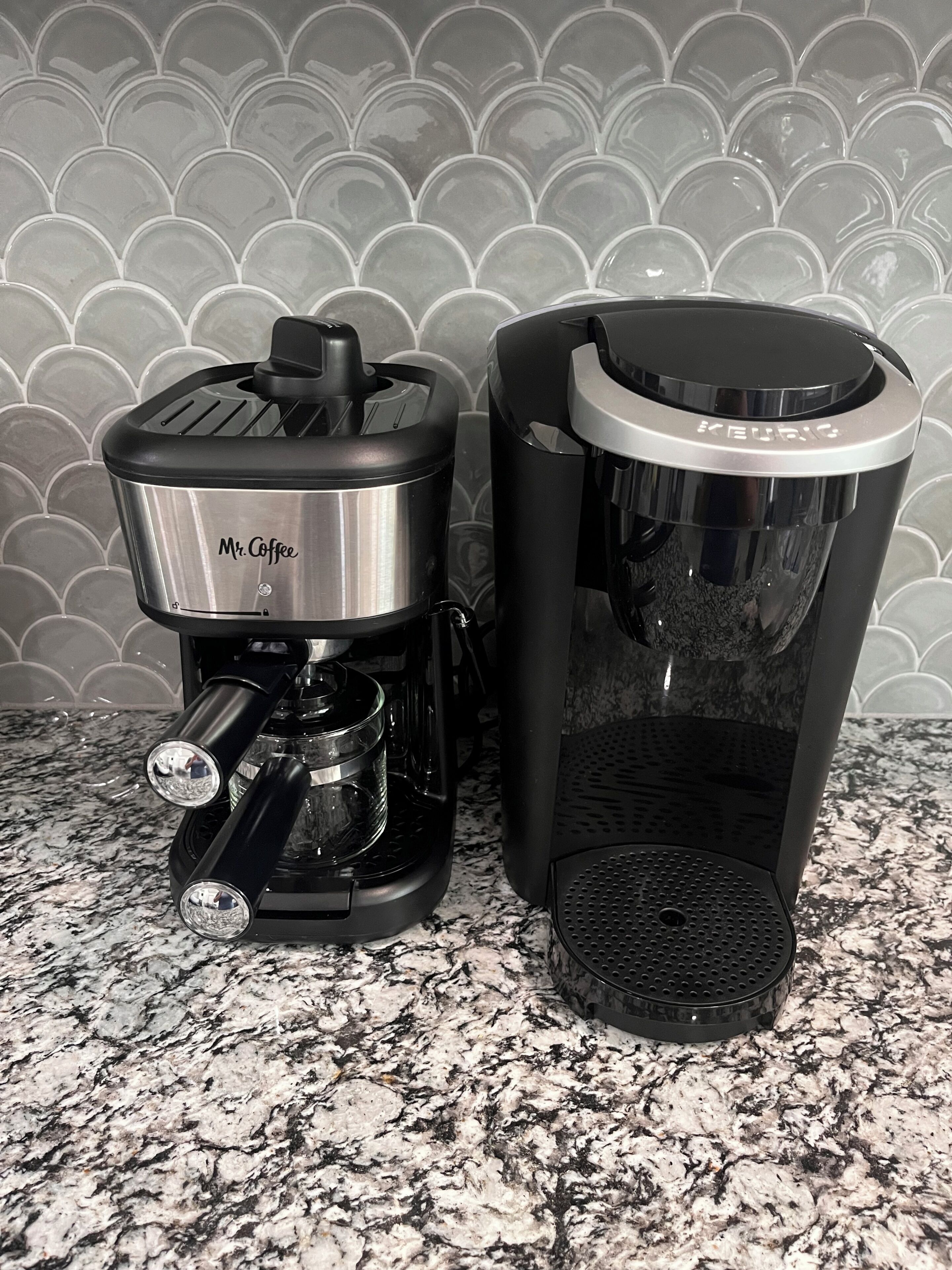 Two coffee makers on a granite countertop with a tiled backsplash.