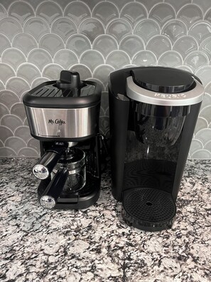 Deux machines à café sont posées sur un plan de travail en granit, avec un pare-feu en carreaux.