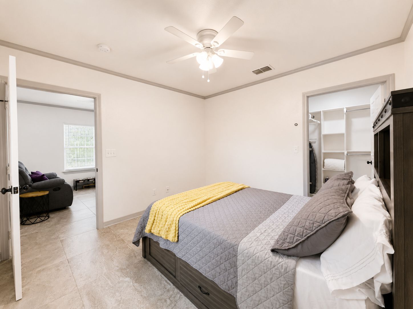 A bedroom with a bed, a ceiling fan, a wardrobe, and a door leading to another room.