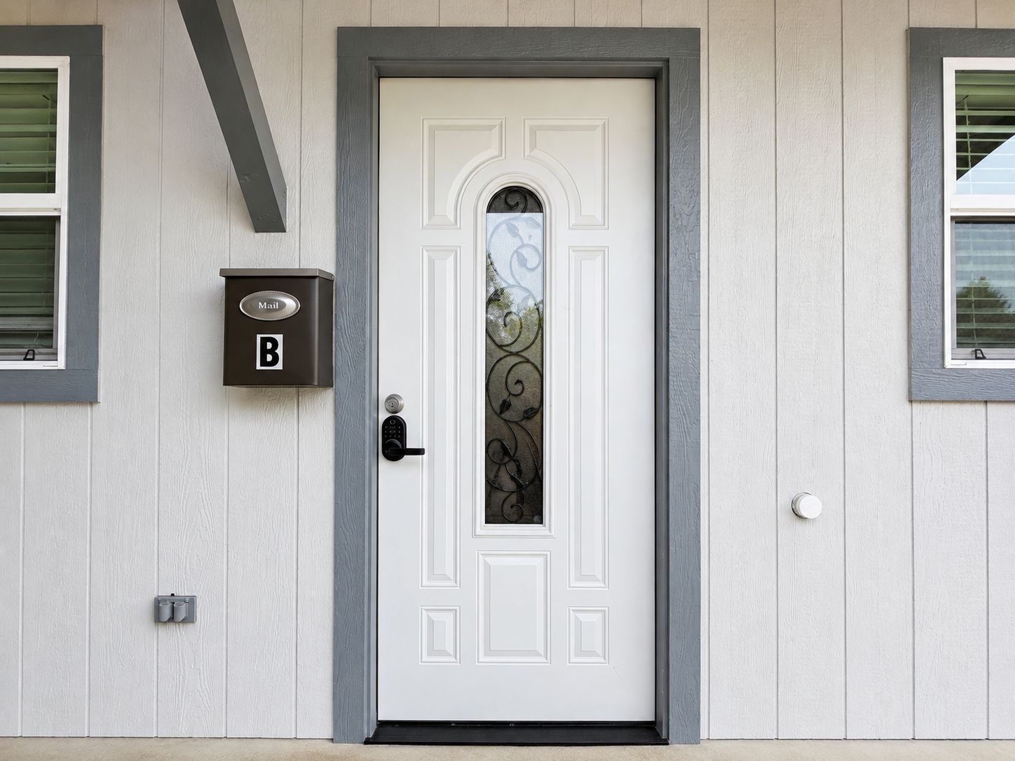 Una porta bianca con un pannello di vetro decorativo, una fessura per la posta e un citofono.