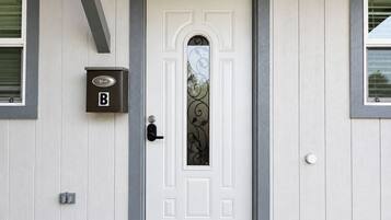 Una porta bianca con un pannello di vetro decorativo, una fessura per la posta e un citofono.