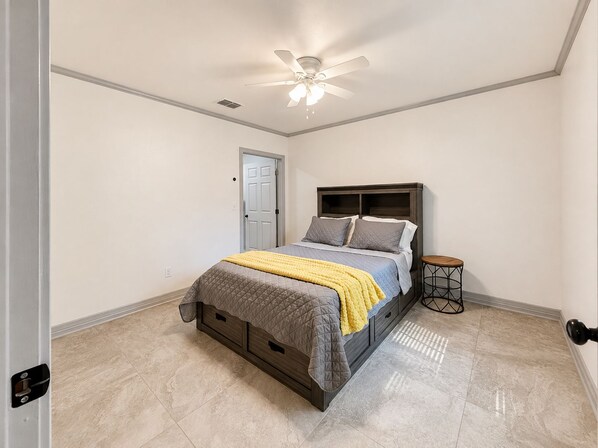 A bedroom with a bed, a bedside table, a ceiling fan, and a door.
