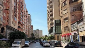 A street lined with multi-story residential buildings, parked cars, and a clear sky. - Bright and Cozy Apartment in a Central Location (Béjaïa)