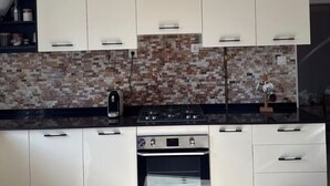 A kitchen with white cabinets, a gas stove, an oven, and a backsplash with a mosaic tile design. - Bright and Cozy Apartment in a Central Location (Béjaïa)