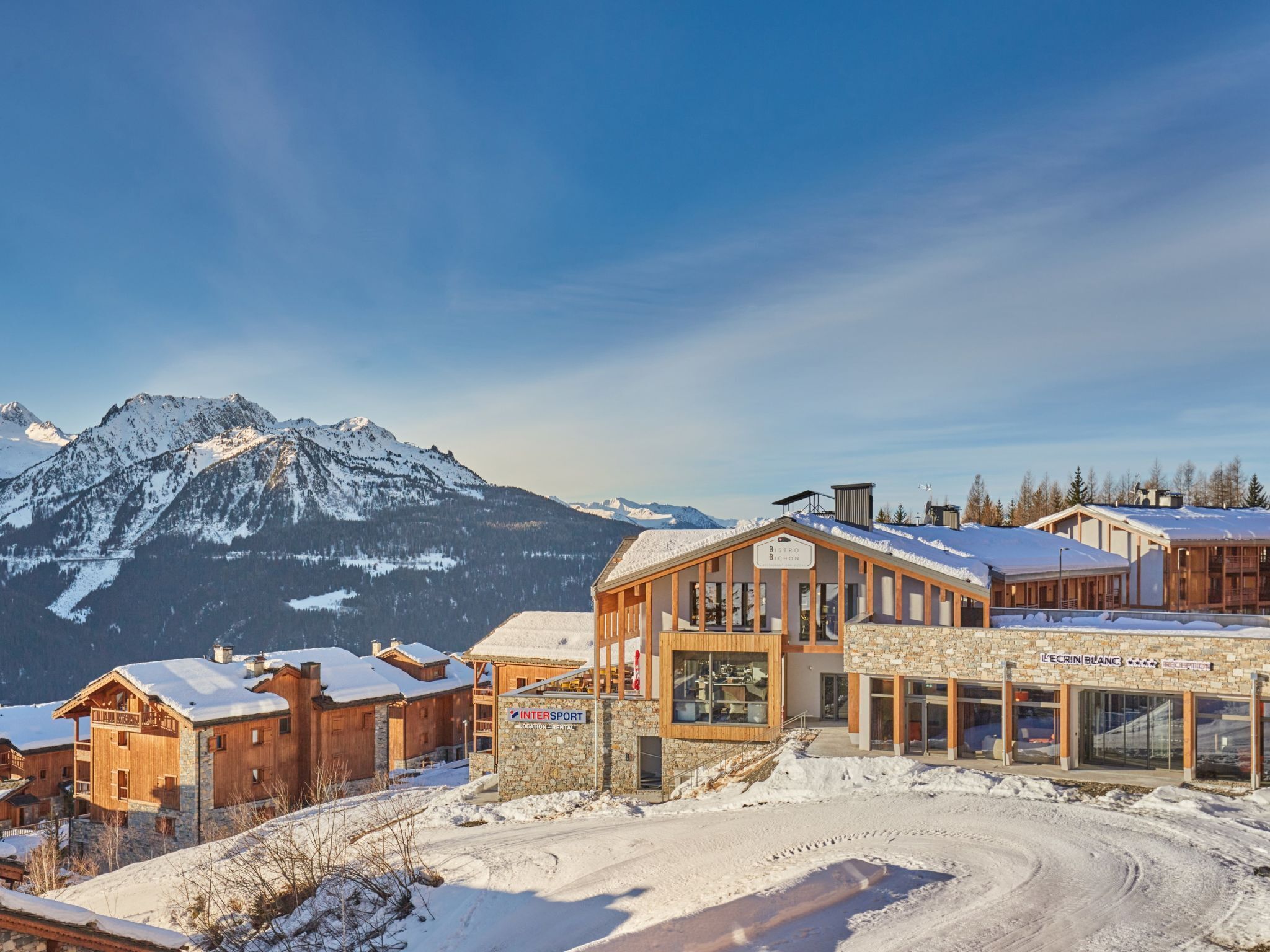 Un chalet de montagne à l’architecture en bois, doté d’une entrée en pierre et offrant une vue sur des montagnes enneigées.