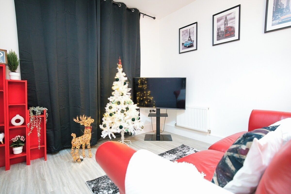 Una sala de estar con un sofá rojo, un árbol de Navidad blanco, una estantería roja y un televisor de pantalla plana.
