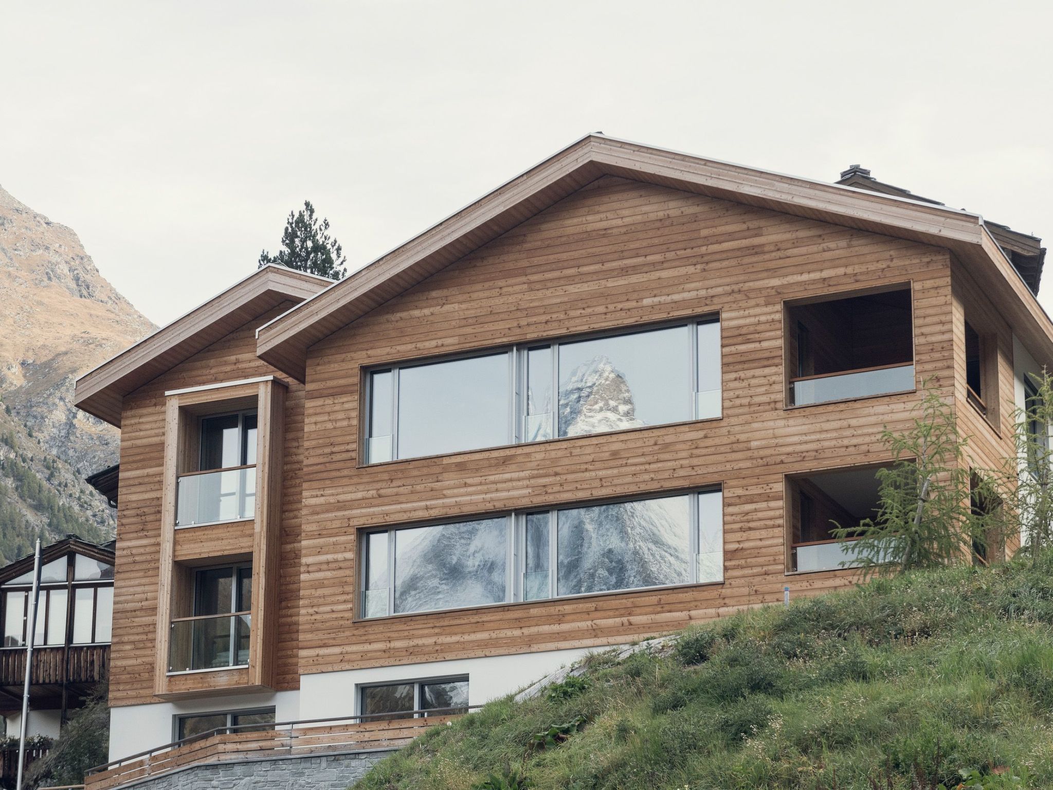 A modern wooden house with large windows and a stone base.