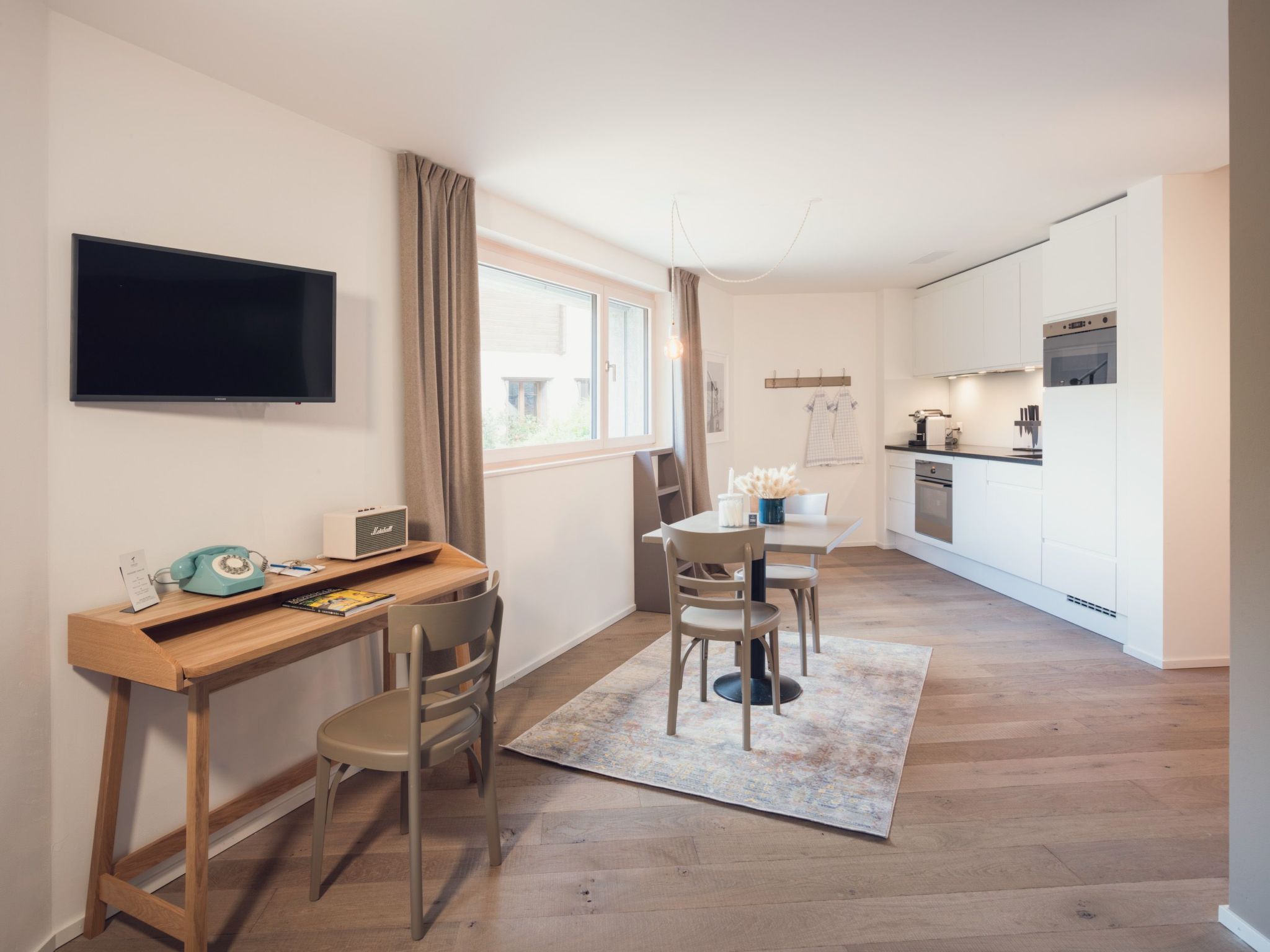A compact living space with a dining area, kitchenette, and a TV mounted on the wall.