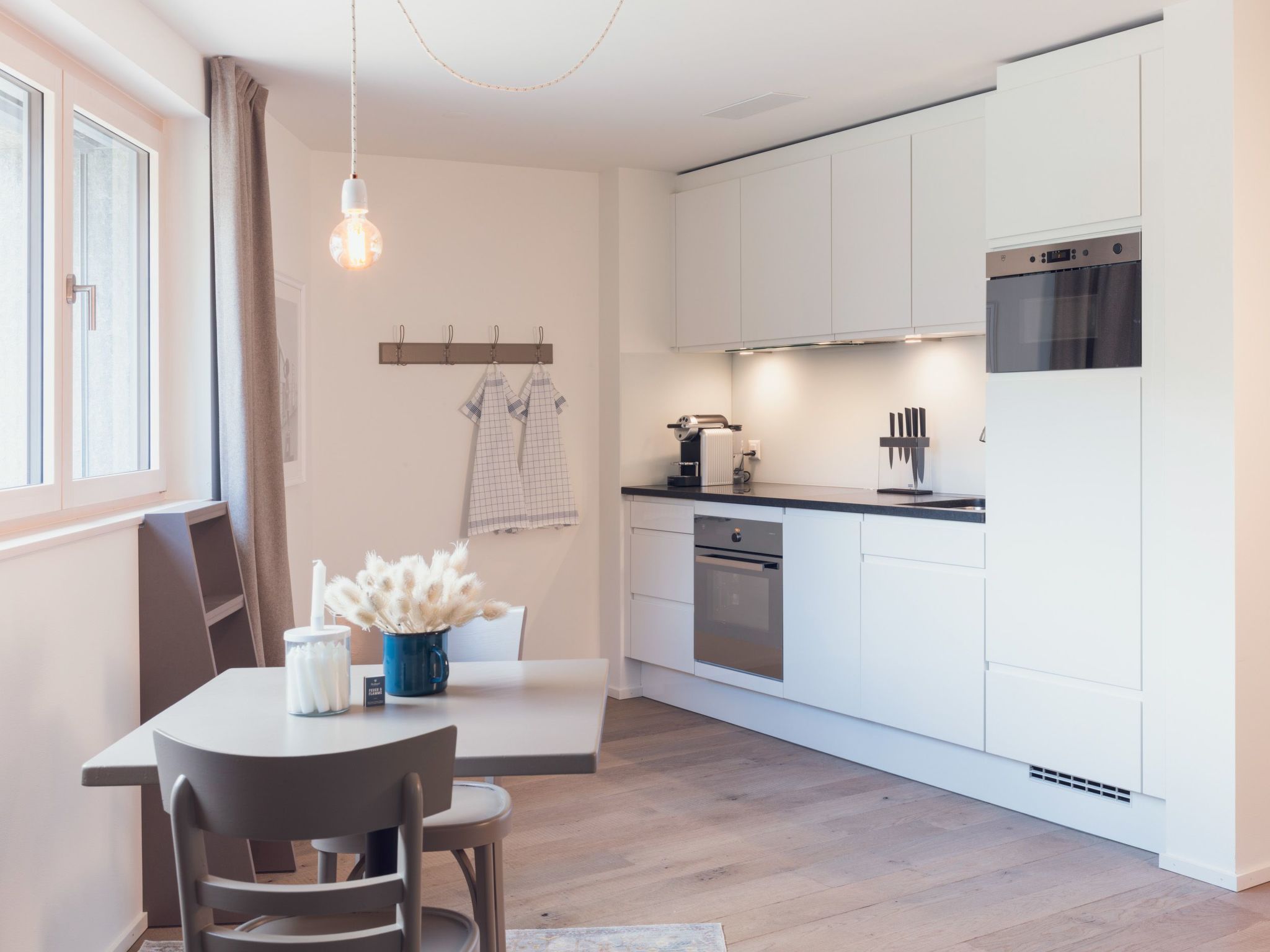 Una cucina moderna con mobili bianchi, forno integrato e zona pranzo con tavolo e sedie.