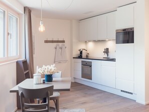 A modern kitchen with white cabinets, a built-in oven, and a dining area with a table and chairs. - OVERLOOK Lodge by CERVO Zermatt, (Zermatt), by Interhome (Zermatt)