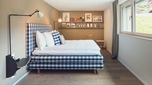 Ein Schlafzimmer mit Bett, Nachttisch, Lampe, einem Regal mit Bildern und einem Fenster.