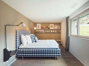 Ein Schlafzimmer mit Bett, Nachttisch, Lampe, einem Regal mit Bildern und einem Fenster.