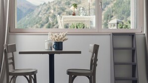 Ein Zimmer mit Tisch und zwei Stühlen, ein Fenster mit Bergblick, eine Leiter und ein kleiner Tisch mit Vase und Pflanze.