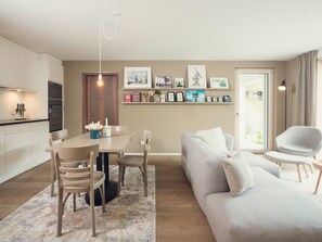 A modern living room with a sofa, chairs, a dining table, and a kitchen area with cabinets and appliances. - OVERLOOK Lodge by CERVO Zermatt, (Zermatt), by Interhome (Zermatt)