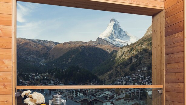 Una finestra con cornice in legno che si affaccia su una montagna e un villaggio sottostante.