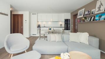 A modern living room with a grey sofa, two armchairs, a coffee table, and a kitchen in the background.