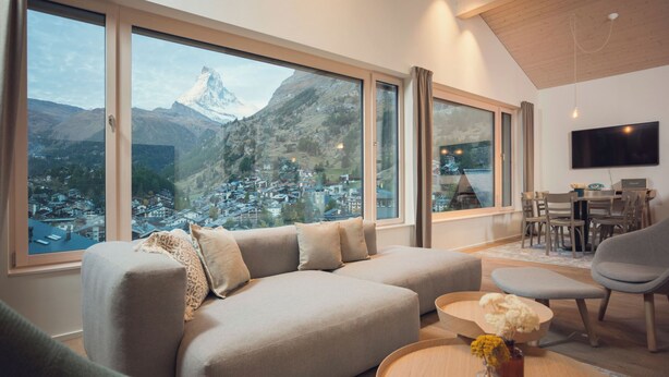 Un soggiorno moderno con un'ampia finestra che si affaccia su una vista montana, un divano, un tavolino da caffè e una zona pranzo.