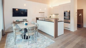 Una cucina moderna con un'isola centrale, un'area pranzo con sedie, una TV a parete e un soffitto in legno.