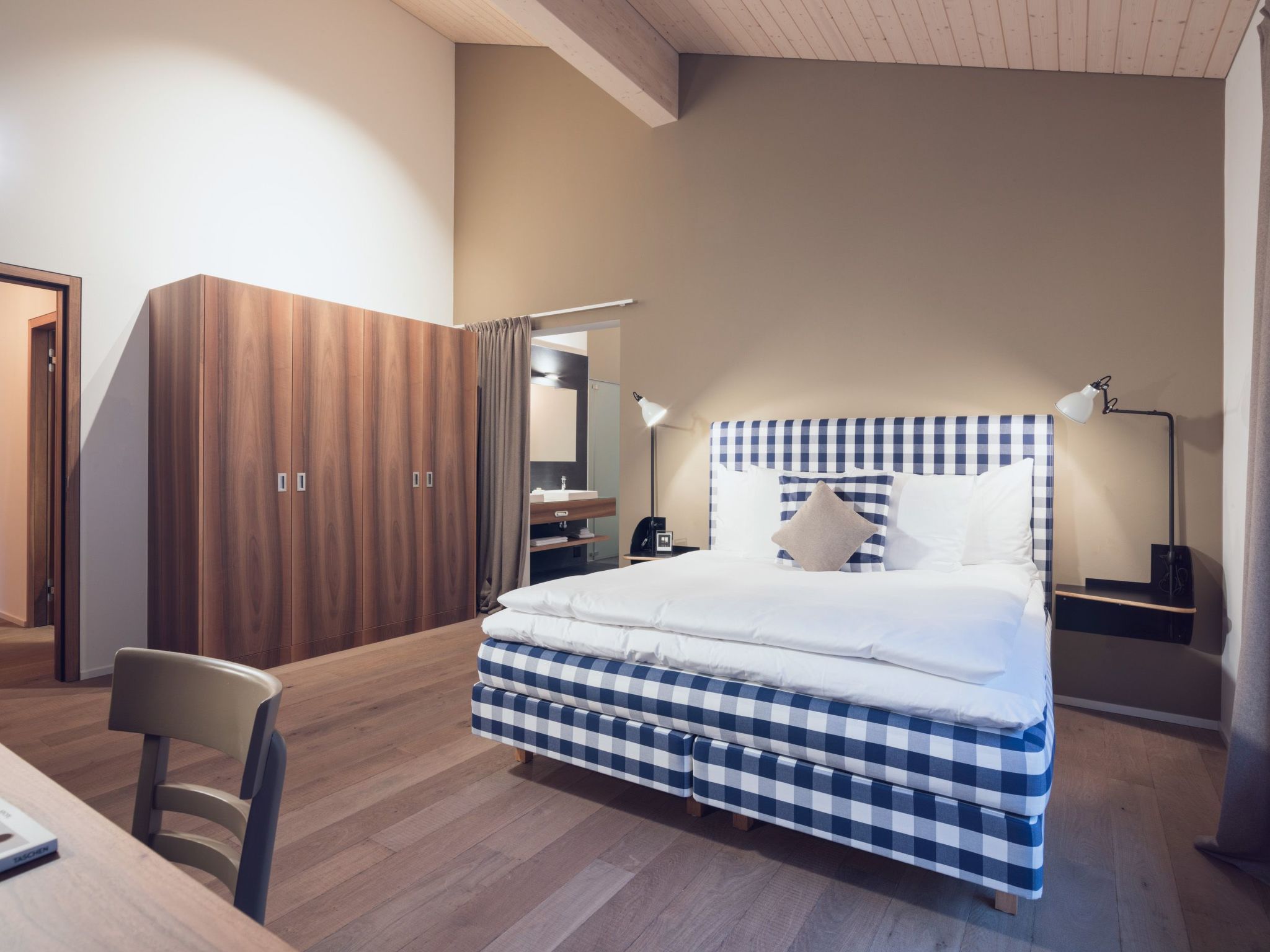 Una camera da letto moderna con una coperta a quadri, una scrivania con una sedia, un armadio e un comodino con una lampada.