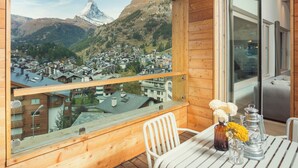 Un balcone in legno con vista su una cittadina in montagna e una vetta imponente.