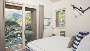 Una camera da letto con un letto, un comodino, una lampada, una finestra e vista su un borgo montano.