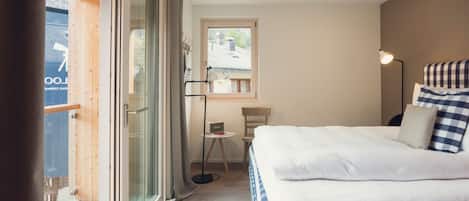 Un dormitorio con cama, escritorio, silla, lámpara y puerta corrediza de vidrio que da a un espacio exterior.