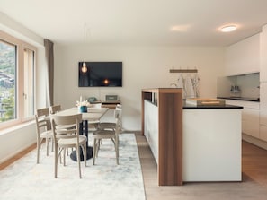 A modern kitchen with a central island, a dining area with chairs, and a flat-screen TV mounted on the wall. - OVERLOOK Lodge by CERVO Zermatt, (Zermatt), by Interhome (Zermatt)