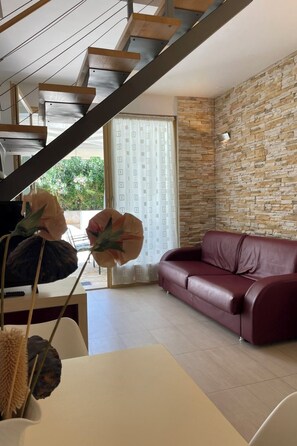Un saló modern amb una paret de pedra, un sofà de cuir vermell i una escala amb graons de fusta.