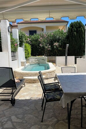 Um pátio externo com banheira de hidromassagem, paredes de pedra e uma mesa com cadeiras.