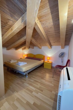 Quarto com cama, mesas de cabeceira, uma cadeira e ar condicionado.