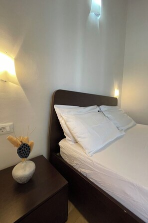 A neatly made bed with white linens, a dark headboard, and a bedside table with a decorative object. - Vacation home Volme by Interhome (Pula/Banjole)