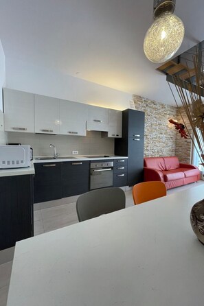 A modern kitchen with a dining area, featuring a stone accent wall, a red sofa, and a unique hanging light fixture. - Vacation home Volme by Interhome (Pula/Banjole)