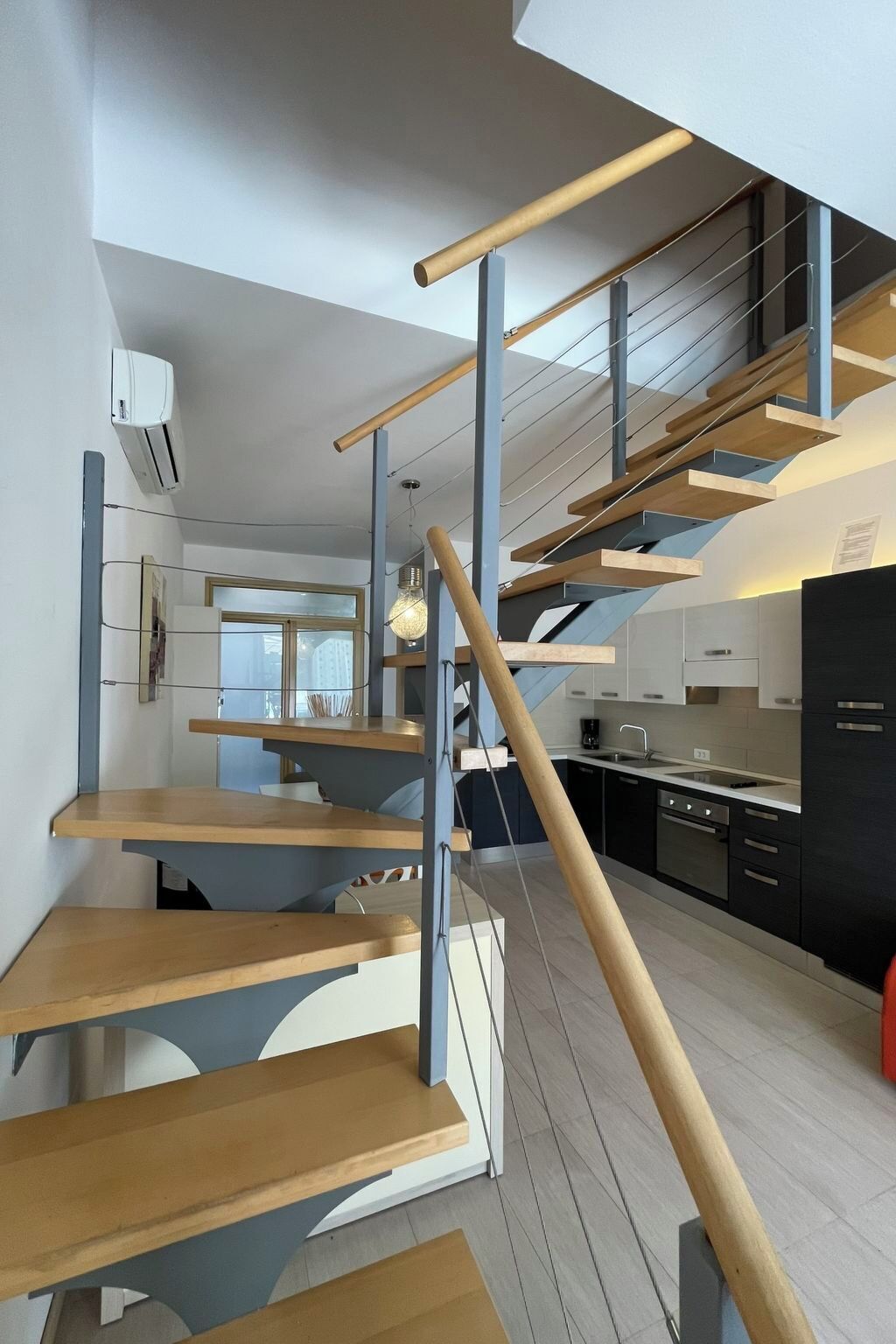 A modern kitchen with a wooden staircase and a view of the city.