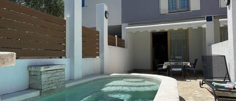 A residential property with a swimming pool, outdoor seating, and a covered patio area.