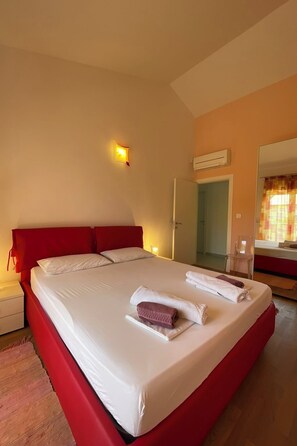 Ein Hotelzimmer mit einem großen Bett, einem Nachttisch, einem Spiegel und einer Klimaanlage.
