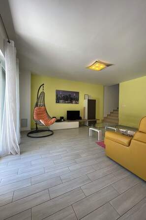 Ein modernes Wohnzimmer mit Hängekorbschaukel, gelbem Sofa, Flachbildfernseher und einer Treppe.