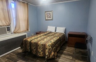 A bedroom with a bed, a nightstand, a dresser, a window with curtains, and a wall-mounted picture.