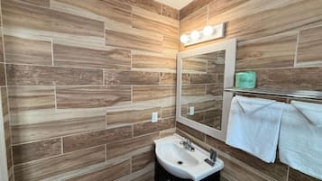 Um banheiro com design de parede de madeira, uma pia, um espelho e um porta-toalhas.