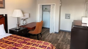 A hotel room with a bed, a desk, a chair, a lamp, a wardrobe, and a door leading to a bathroom.
