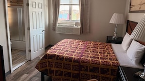 A hotel room with a bed, a bedside table, a lamp, a window with curtains, and a door.