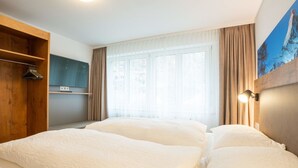 Habitación de hotel con dos camas, un televisor, un armario de madera y una ventana con cortinas.