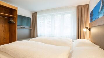 Ein Hotelzimmer mit einem großen Bett, einem Holzschrank, einem Flachbildfernseher und einem Fenster mit Vorhängen.