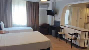 Habitación de hotel con dos camas, un escritorio, una silla, un televisor y una kitchenette pequeña.