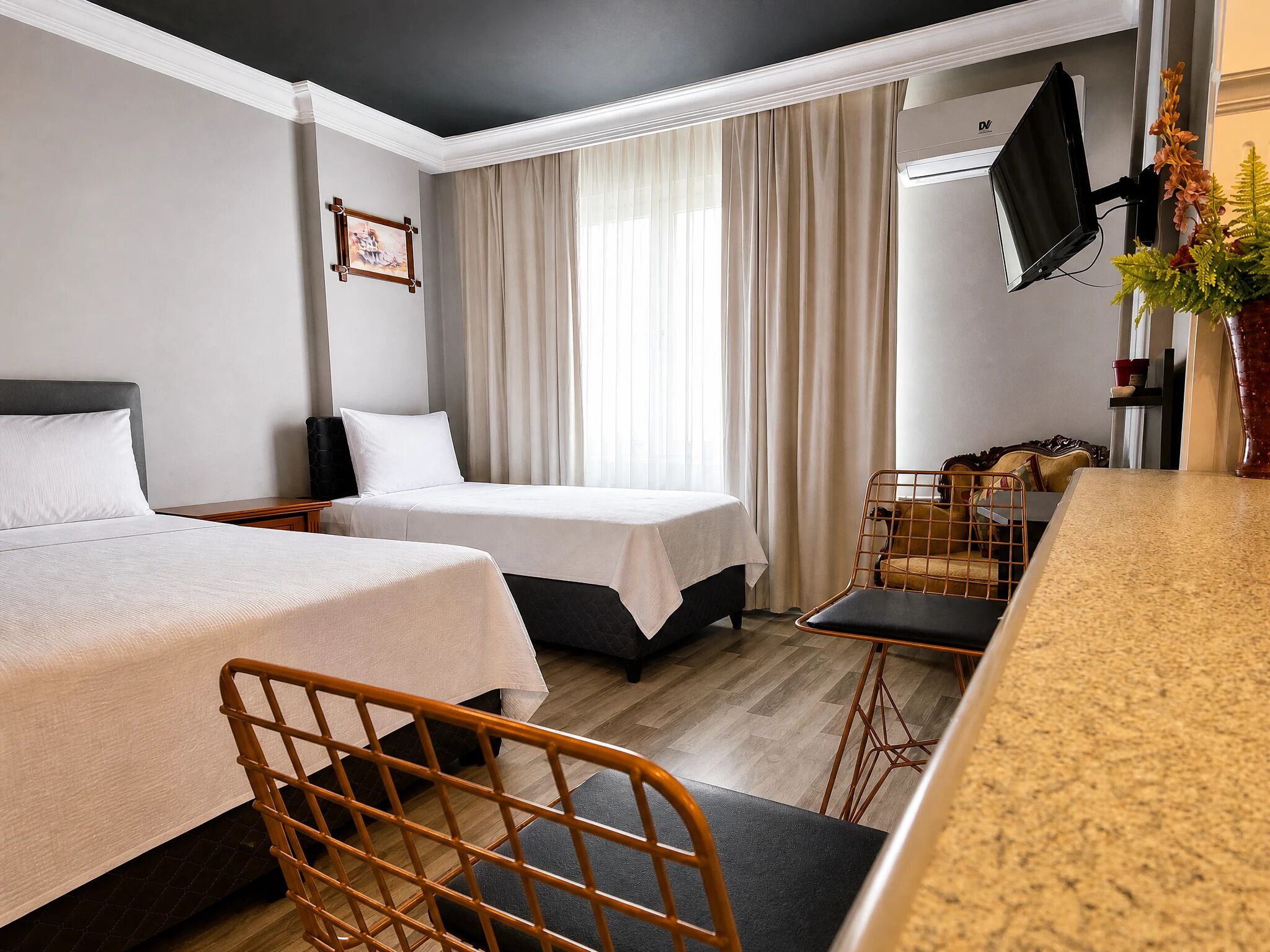 A hotel room with two beds, a desk, a chair, a TV, and a window with curtains.