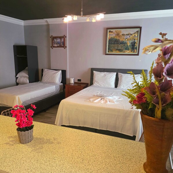 A hotel room with two beds, a nightstand, a painting on the wall, and a potted plant.