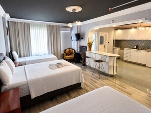 Una habitación de hotel moderna con dos camas, una zona de estar, un televisor y una kitchenette.