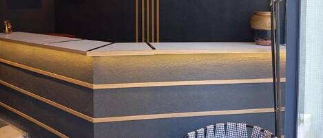 Un mostrador de recepción con una pared oscura, una obra de arte enmarcada, un reloj y una lámpara decorativa.