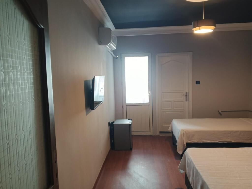A room with two beds, a small trash bin, a door, and a window.