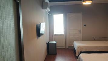 A room with two beds, a small trash bin, a door, and a window.